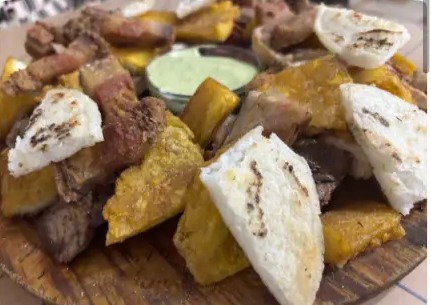 Tabla de madera con picada de carnes, chicharrón, patacón, arepa y salsa verde
