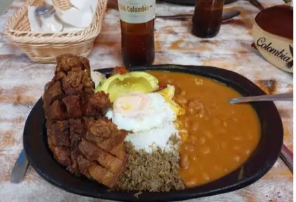 Bandeja paisa servida en plato de barro con frijoles, arroz, huevo frito, chicharrón y arepa