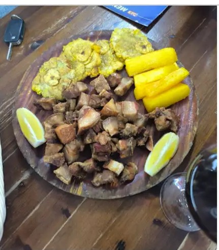 Tabla de madera con patacones de plátano verde, yuca frita, chicharrón y limón